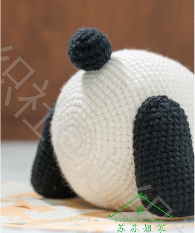 close up detailed 45 degree view of the right side of butt of crochet panda plushie amigurumi, panda's white butt is very round with ball shaped black tail stuck on butt, two short chungky legs at both sides, panda resting on colored table