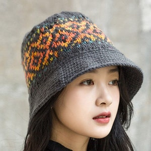 May include: A gray crocheted bucket hat with a colorful geometric pattern. The hat has a wide brim and is made of a soft, textured yarn.