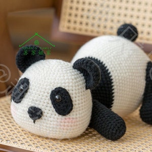 left side front view of crochet panda amigurumi/plushie lying on tummy on ratten weaven chair, panda bear in black and white, round face, round butt and tail sticking up in air , short arms and legs, with indoor background