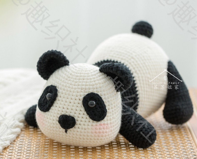 front view of cute panda stuffing panda amigurumi resting on bamboo meshed surface with tummy, panda's butt lifted in the air, with grey background