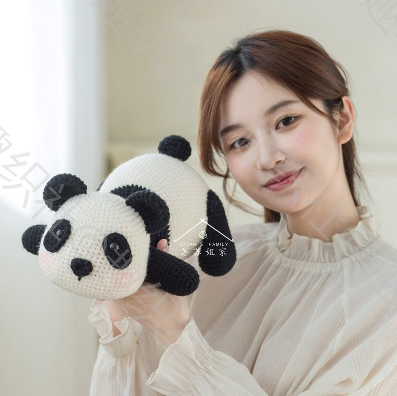 young Chinese female model holding panda amigurumi/toy/doll, panda at her front right, panda facing camera, panda in lying posture, with indoor background