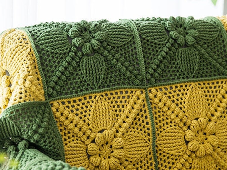 close up details of Victorian-Style floral granny square couch cover, patches in dark green and ginger yellow colors, joined with dark green crochet stitches, pop-corn stitches/symbols are frequently used