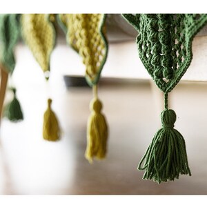 close up details for tessels hung from triangle crochet patches, patches in yellow and dark green colors with Victorian style granny square floral pattern, with table surface background