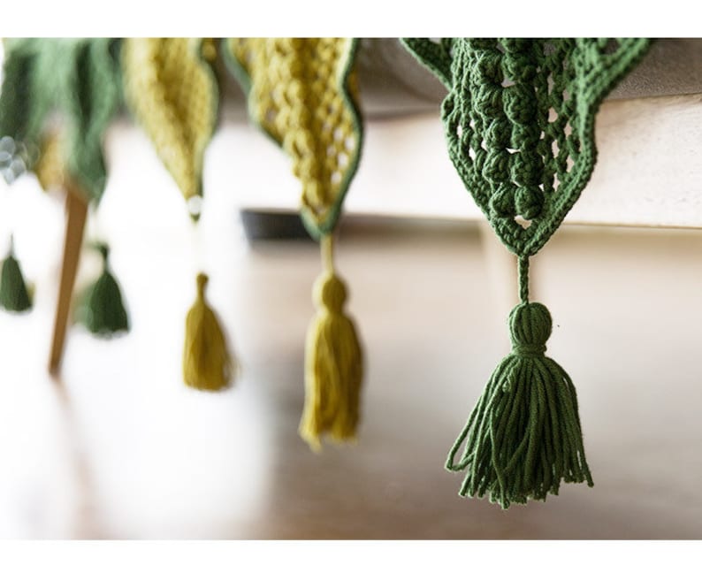 close up details for tessels hung from triangle crochet patches, patches in yellow and dark green colors with Victorian style granny square floral pattern, with table surface background