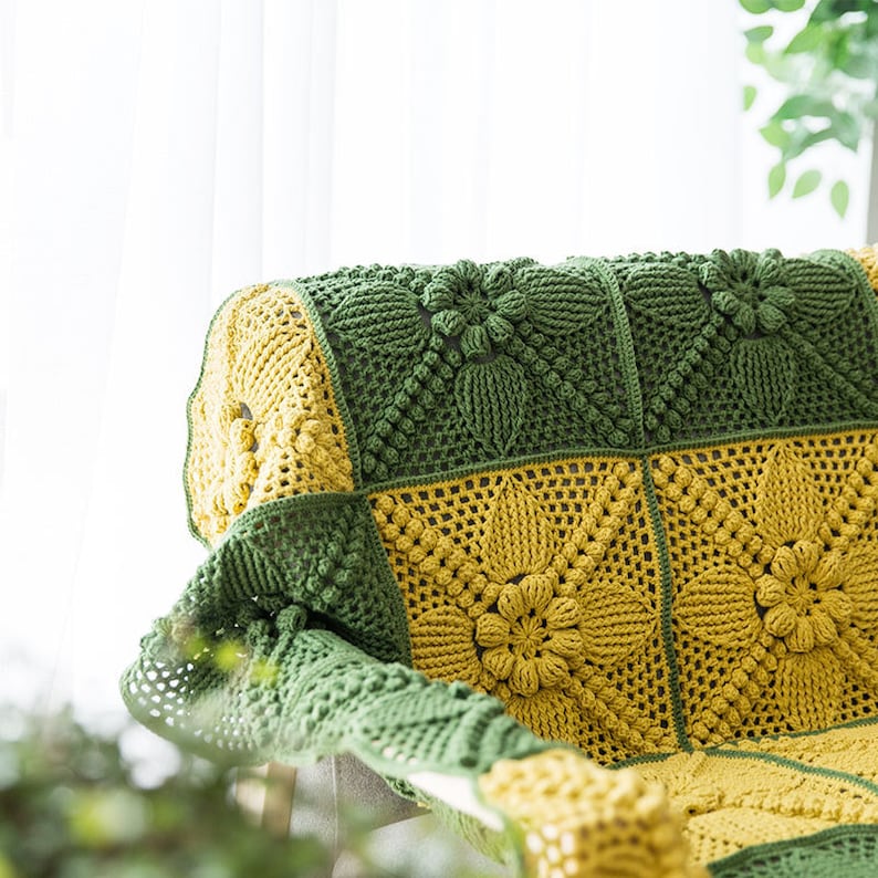 close up details of crochet sofa cover. cover made of green and ginger yellow, floral, victorian style granny square blocks, with a lot of pop corn motif, with indoor background