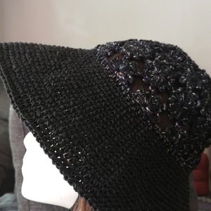 May include: A black crochet sun hat with a wide brim and a decorative trim of black and purple flowers.