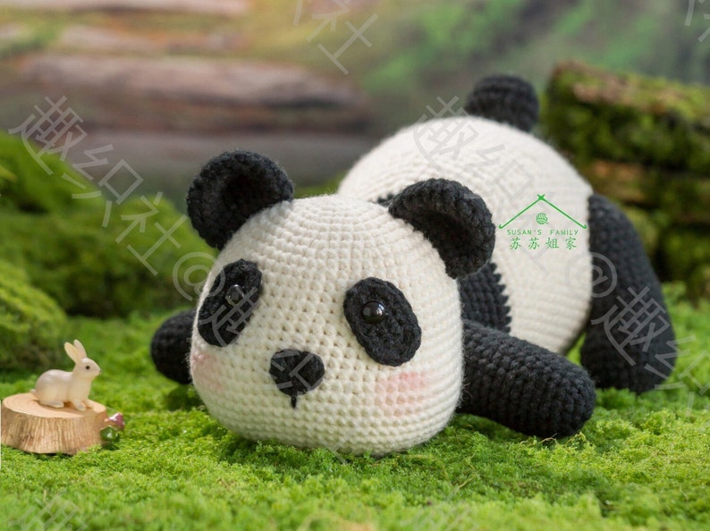 cute crochet panda lying on grassland with tummy facing camera by 45 degree angle, panda having big uprising butt, panda looking at tiny rabbit in front of him, with mountain background