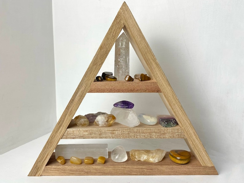 May include: A wooden triangular shelf with three tiers, displaying a variety of crystals and stones, including clear quartz, amethyst, tiger's eye, and citrine.