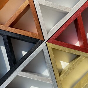 May include: A geometric wall art piece made of six triangles in different colors. The triangles are arranged in a pattern that creates a star shape. The colors of the triangles are copper, black, silver, red, gold, and white.