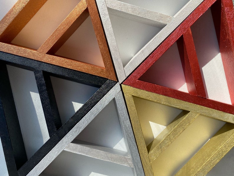 May include: A geometric wall art piece made of six triangles in different colors. The triangles are arranged in a pattern that creates a star shape. The colors of the triangles are copper, black, silver, red, gold, and white.