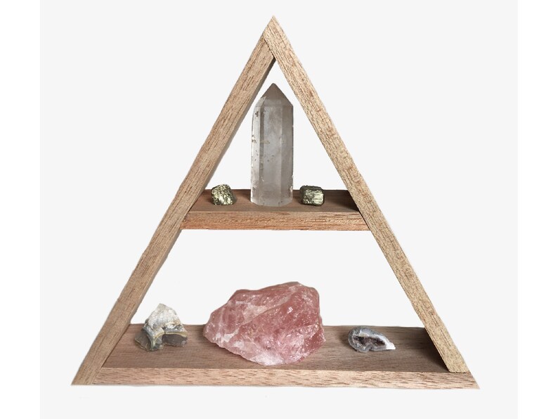 May include: A wooden triangular shelf with two shelves, displaying various crystals and stones. The top shelf has a clear quartz crystal and two gold pyrite stones. The bottom shelf has a large rose quartz crystal, a small clear quartz crystal, and a gray agate stone.