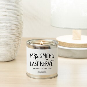 Pu&ograve; includere: Una lattina di candela argentata con un'etichetta bianca che recita "Mrs. Smith's Last Nerve" e "Oh look... it's on fire." La candela &egrave; accesa e la fiamma &egrave; visibile.