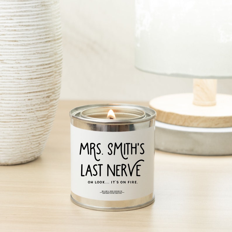 Pu&ograve; includere: Una lattina di candela argentata con un'etichetta bianca che recita "Mrs. Smith's Last Nerve" e "Oh look... it's on fire." La candela &egrave; accesa e la fiamma &egrave; visibile.