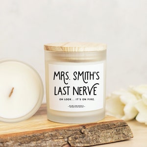 Pu&ograve; includere: Un barattolo di vetro bianco smerigliato per candele con un coperchio in legno. La candela ha un'etichetta bianca con testo nero che recita "MRS. SMITH'S LAST NERVE OH LOOK... IT'S ON FIRE."