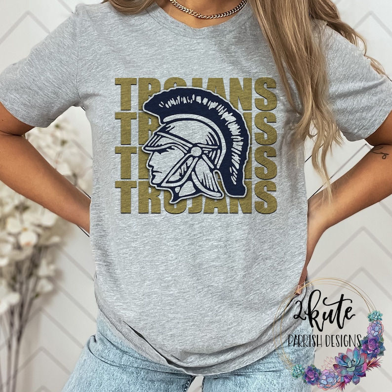 K&ouml;nnte beinhalten: Ein graues T-Shirt mit einer goldenen Grafik eines r&ouml;mischen Kriegerkopfes mit Helm und dem Wort "Trojans", das viermal wiederholt wird.