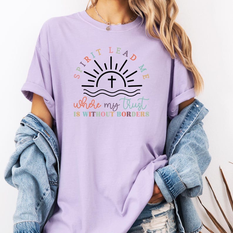 May include: A lavender t-shirt with a graphic of a sunrise with a cross and the text "Spirit Lead Me where my trust is without borders".