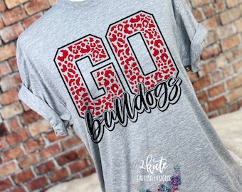 Op de afbeelding: Een heather grijze t-shirt met opgerolde mouwen. De shirt toont de woorden "GO BULLDOGS" in een zwart-wit script, met de letters "GO" gevuld met een rood luipaardprint ontwerp. Een logo is zichtbaar aan de onderkant.