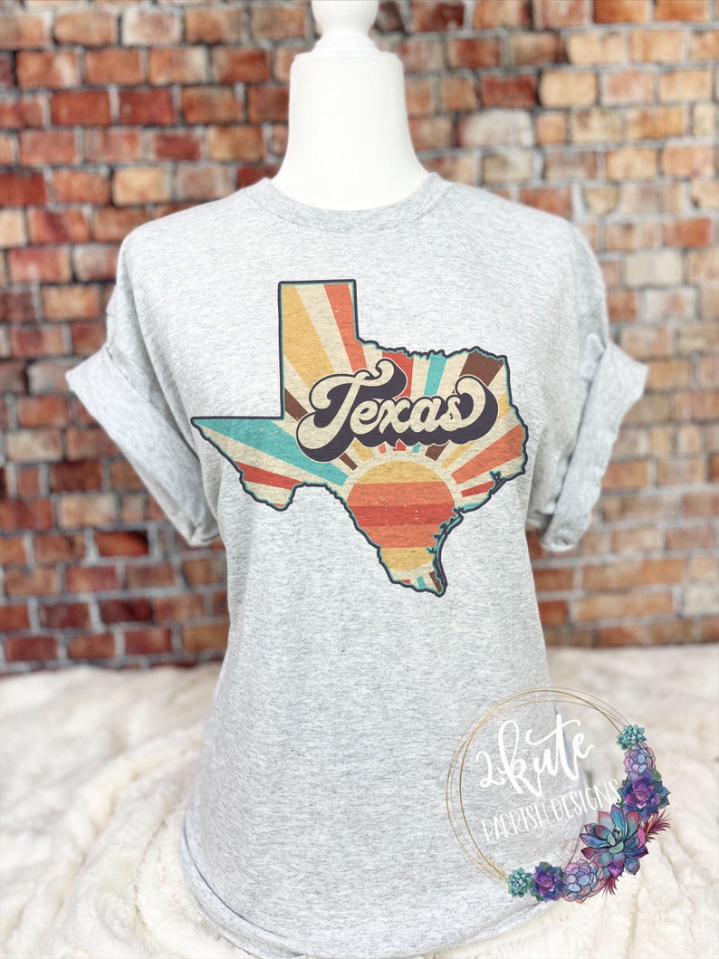May include: A grey t-shirt featuring a vintage-style graphic of the state of Texas. The graphic has a sunburst design with the word "Texas" in a retro font.