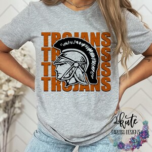 Pu&ograve; includere: Maglietta grigia con la parola "Trojans" ripetuta quattro volte in testo arancione. Un'illustrazione in bianco e nero di un elmo da guerriero troiano &egrave; centrata sulla maglietta.