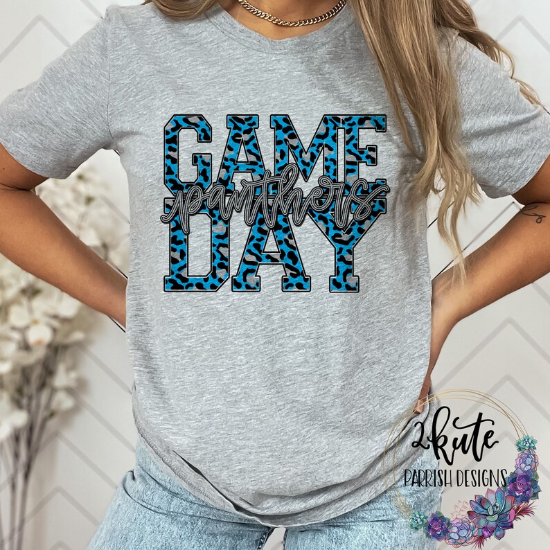 May include: Gray t-shirt with a blue and gray leopard print design that says "GAME DAY" with the word "Panthers" in a smaller font in between the words "GAME" and "DAY".