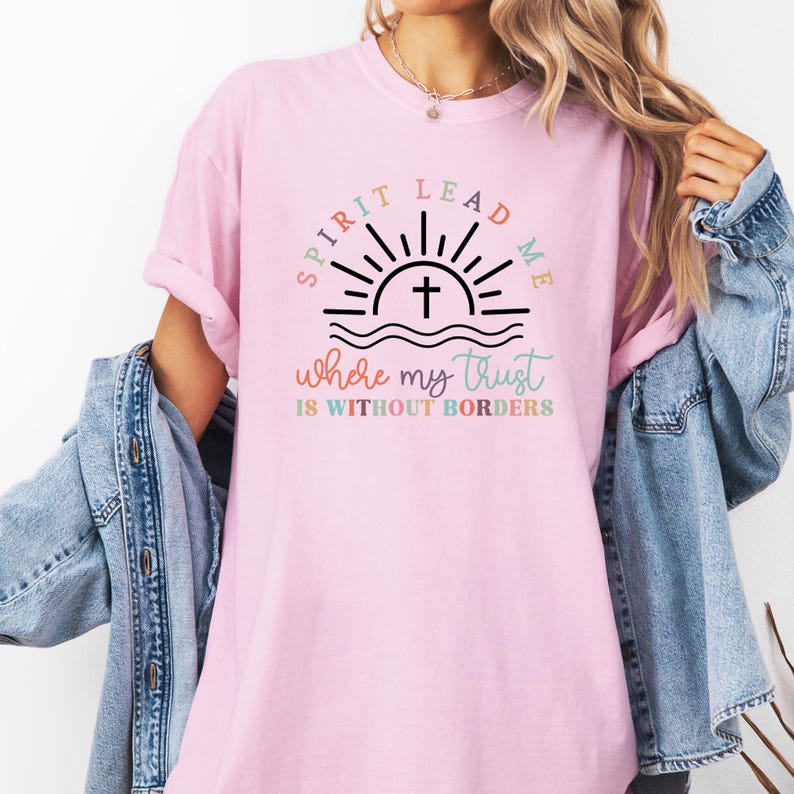 May include: Pink t-shirt with a graphic design of a sunrise with a cross in the center. The text reads "Spirit Lead Me where my trust is without borders".