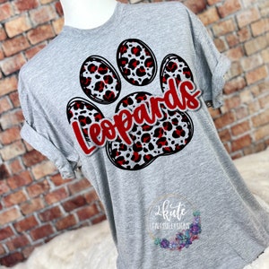 May include: A gray t-shirt featuring a paw print design with red and black leopard print accents. The word "Leopards" is written in red script across the paw print. The shirt has rolled-up sleeves.