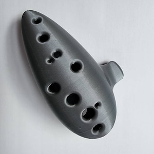 May include: A gray ceramic ocarina with eight finger holes. The ocarina is a musical instrument that is played by blowing into a mouthpiece and covering the holes with the fingers.