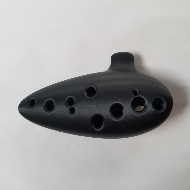 May include: A black ocarina with multiple finger holes. The ocarina is a wind instrument.