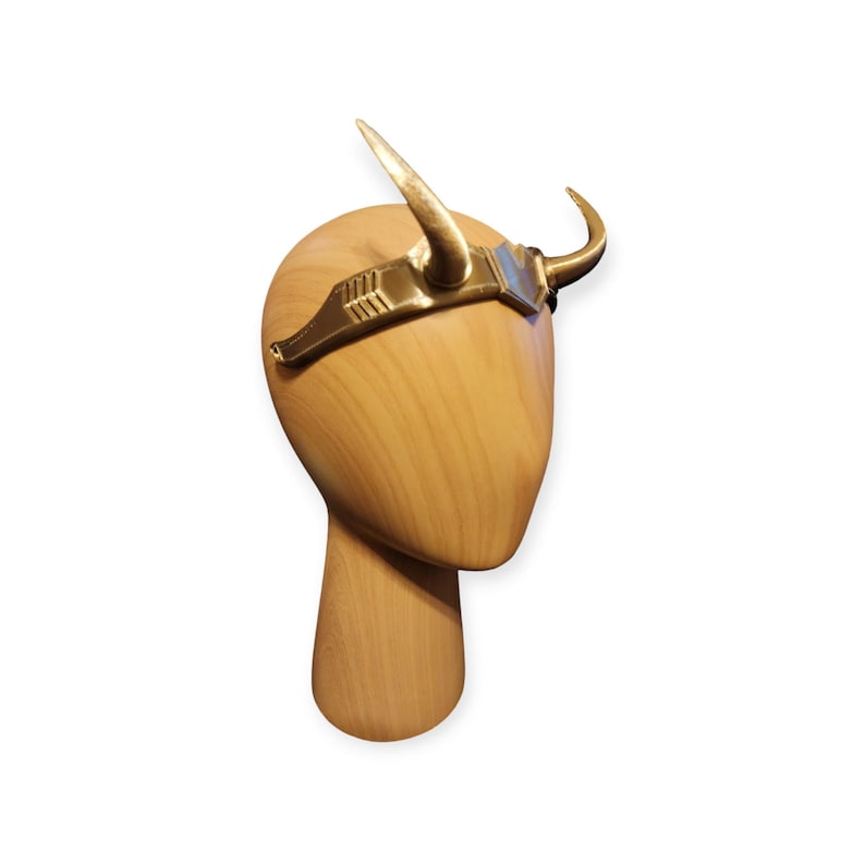 May include: Gold headband with two horns, worn on a wooden mannequin head.