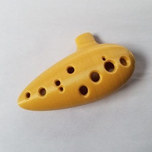 May include: A yellow ocarina with eight finger holes. The ocarina is a wind instrument.