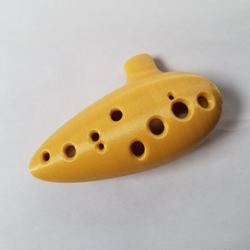 May include: A yellow ocarina with eight finger holes. The ocarina is a wind instrument.