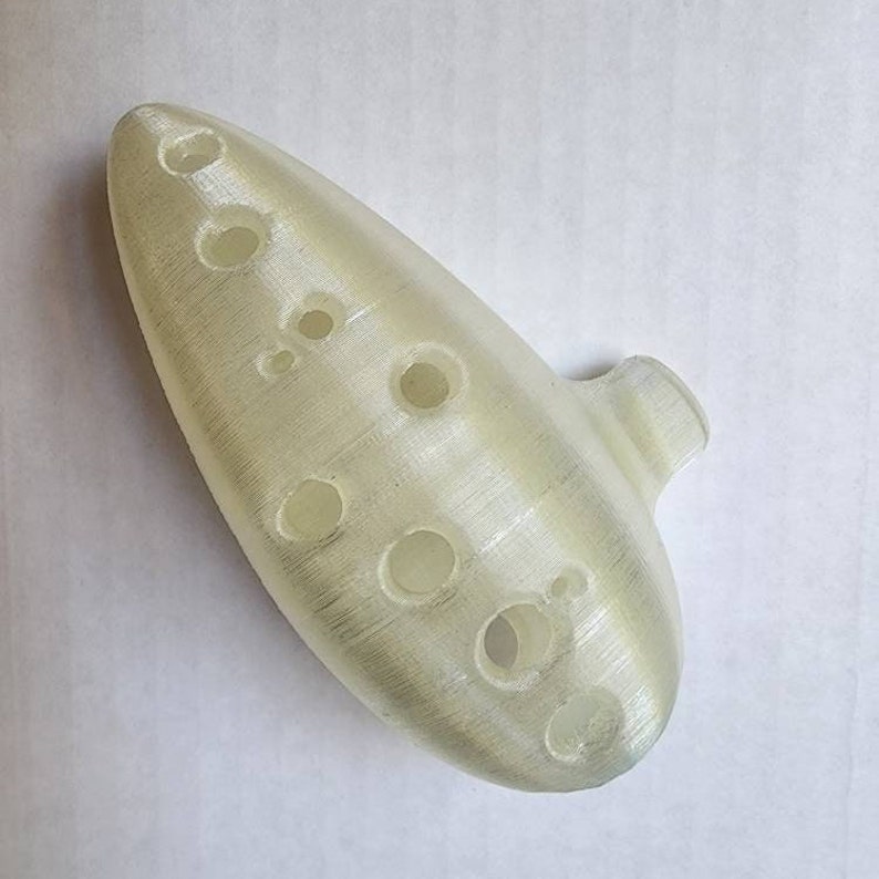 May include: A white ocarina with eight finger holes. The ocarina is made of a smooth, white plastic and has a slightly textured surface.