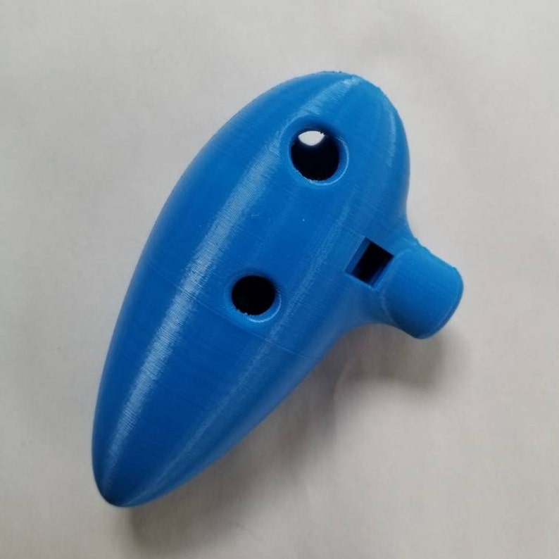 May include: A blue plastic ocarina with four finger holes and a mouthpiece. The ocarina is a wind instrument.