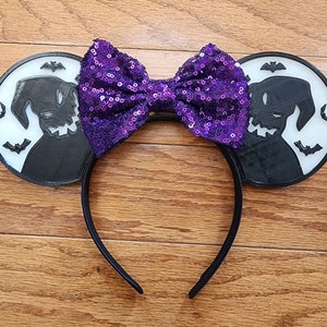 K&ouml;nnte beinhalten: Stirnband mit lilafarbenem Paillettenbogen und schwarzen Ohren, die eine Silhouette von Oogie Boogie aus Nightmare Before Christmas zeigen.