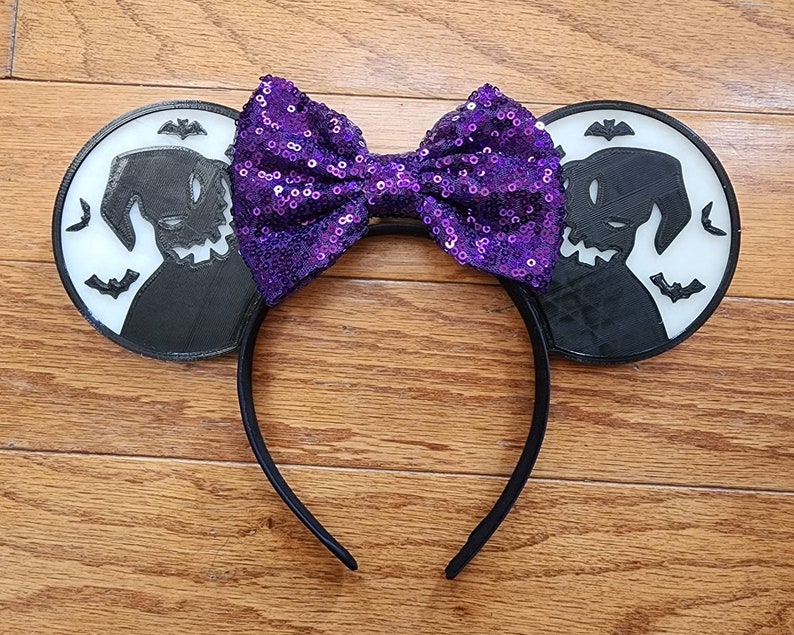 K&ouml;nnte beinhalten: Stirnband mit lilafarbenem Paillettenbogen und schwarzen Ohren, die eine Silhouette von Oogie Boogie aus Nightmare Before Christmas zeigen.