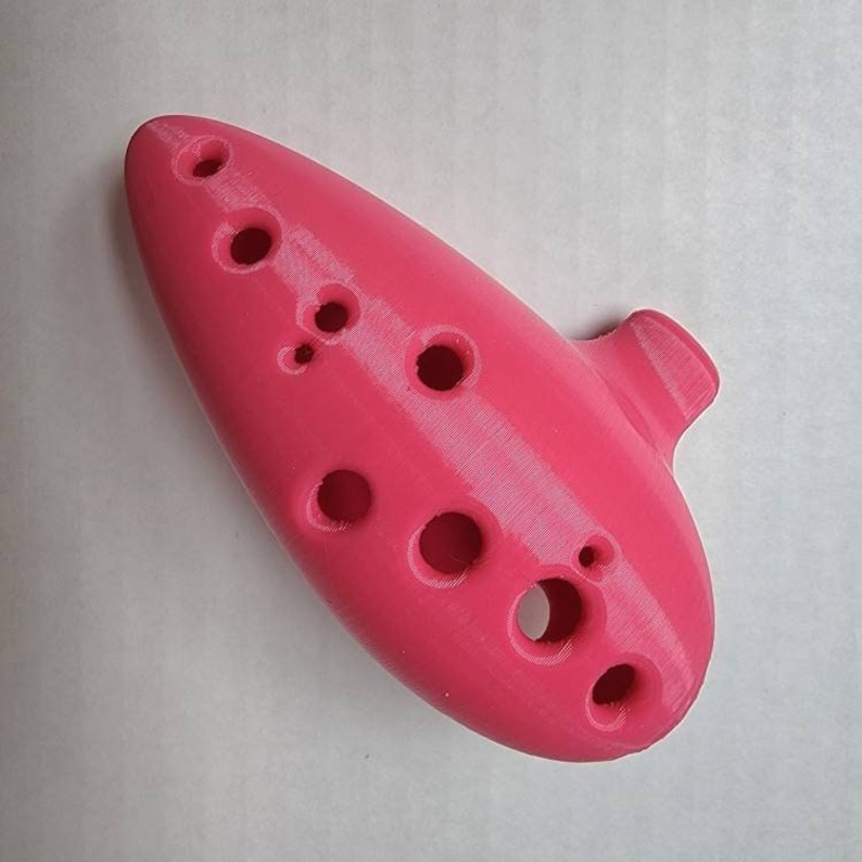 May include: A pink ocarina with eight finger holes. The ocarina is a wind instrument.