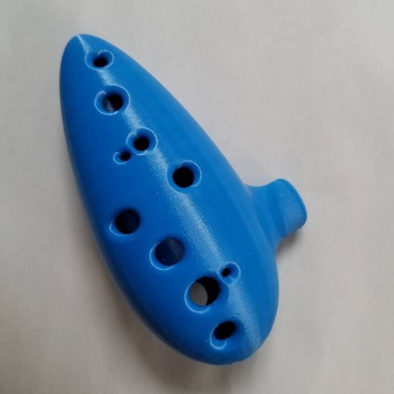 May include: A blue plastic ocarina with eight finger holes. The ocarina is a wind instrument.