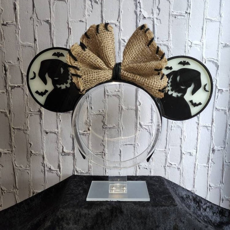 K&ouml;nnte beinhalten: Ein Paar schwarze und wei&szlig;e M&auml;useohren mit einer Schleife aus Sackleinen. Die Ohren zeigen eine Silhouette der Figur Oogie Boogie aus dem Film Nightmare Before Christmas.