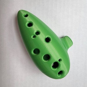 May include: A green ocarina with multiple finger holes. The ocarina is a wind instrument.