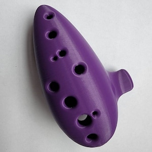 May include: A purple ocarina with eight finger holes. The ocarina is a wind instrument that is often used in fantasy and video games.