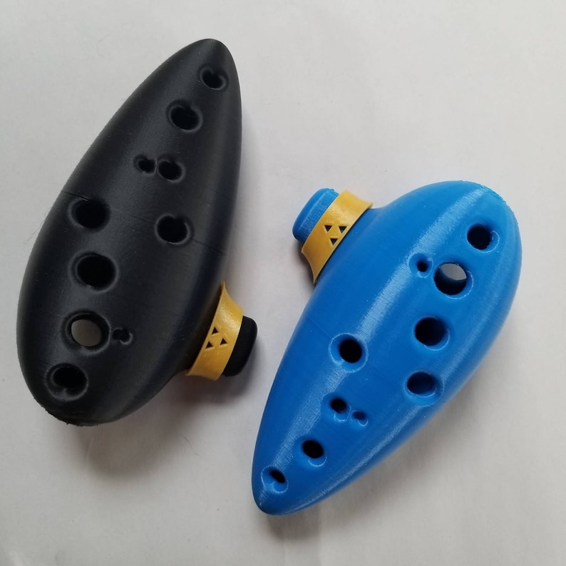 May include: Two ocarinas, one black and one blue, with yellow accents. The ocarinas are made of plastic and have multiple finger holes.