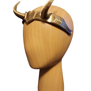 May include: Gold headband with two horns, worn on a wooden mannequin head.