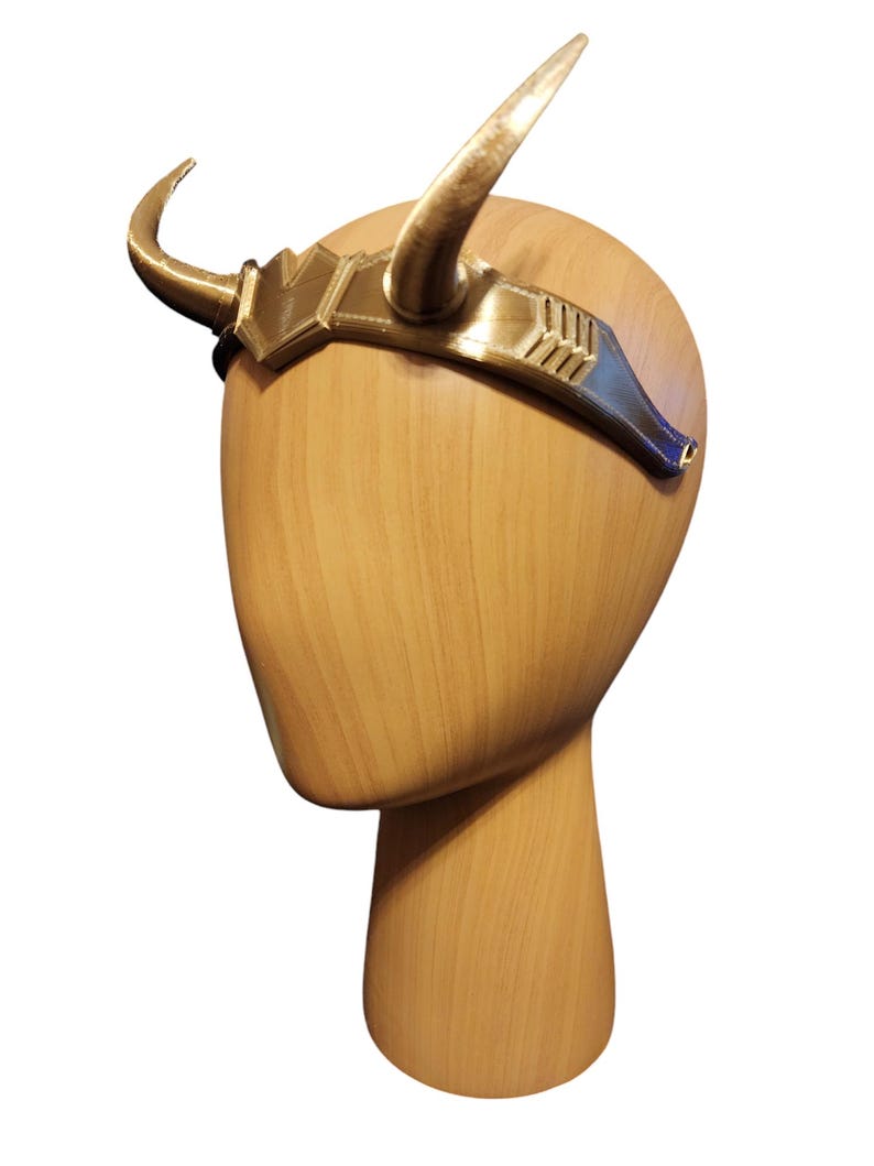 May include: Gold headband with two horns, worn on a wooden mannequin head.