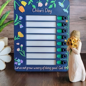 May include: A navy blue decorative board with the text "Chloe's Day" and floral accents. The board has several white rectangular sections and green toggle switches. A small figurine of a woman holding sunflowers is to the right.