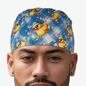May include: A blue and white patterned head covering featuring a repeating design of yellow rubber ducks wearing sunglasses and surrounded by bubbles. The head covering is made of a soft, flexible material.