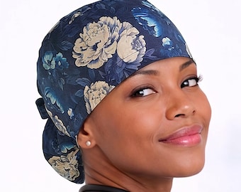 Puede incluir: Un gorro de quirófano azul oscuro con un estampado floral de flores crema y azul claro. El gorro está atado con un nudo en la parte posterior. La persona lleva una camiseta verde de quirófano y un estetoscopio.