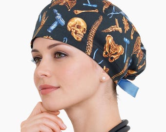 May include: A dark blue surgical scrub cap with a pattern of anatomical illustrations, including bones, a skull, and surgical tools. The cap has a blue tie in the back. Medical theme.