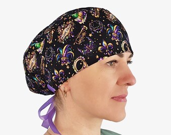May include: A black scrub cap featuring a colorful Mardi Gras print with fleur-de-lis symbols, trumpets, masks, and beads. The cap includes a purple ribbon tie at the back to secure the fit, with the text Mardi Gras printed on the fabric.