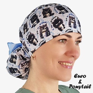 May include: A white and blue Euro & Ponytail scrub cap featuring a repeating pattern of black cat illustrations with the phrase "I'm fine" and a blue bow. The cap is designed for medical professionals.