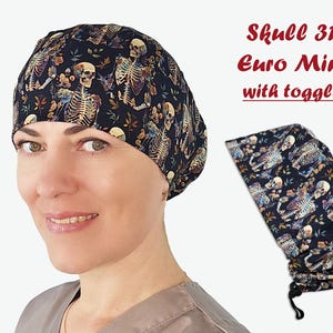 Puede incluir: Un gorro quir&uacute;rgico azul oscuro con un patr&oacute;n repetido de esqueletos y elementos florales. El gorro se muestra en una persona y tambi&eacute;n se muestra por separado. El texto "Skull 31 Euro Mini with toggle" es visible.